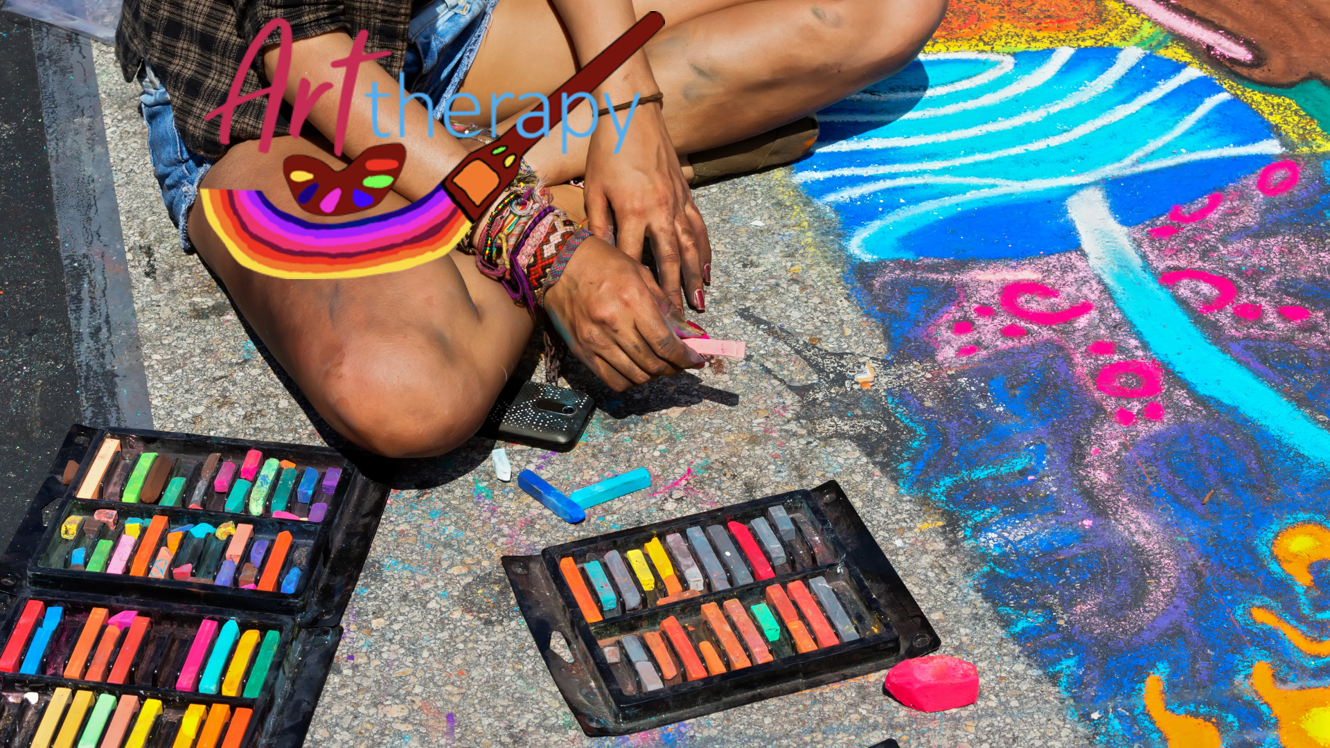 Young man sitting on a pavement, creating images using pastels and charcoals with art therapy now's logo in the top left. This image is used on art therapy now's homepage.